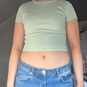 Ljusgrön ribbad croppad topp - Säljer en ljusgrön ribbad croppad topp med korta ärmar. Perfekt för varma dagar och en avslappnad stil. Passar bra med jeans eller kjol.