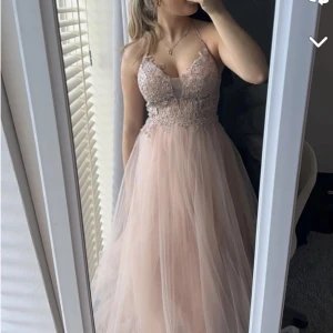 Ljusrosa bal klänning med spets och tyll - Fin ljusrosa långklänning med smala axelband, v-ringad spetsliv och voluminös kjol i tyll. Perfekt till när man har bal eller ska på en fest eller bröllop, den är uppsydd till mig som är 155 men passade när jag hade klackar så passar någon upp till 158, finns inte att köpa längre men köpte för 2500 och det kostande 1000 att sy upp så nypris 3500, säljer för 2000 då en av hasparna där bak är sönder men det finns två på varje ändå, använd en gång