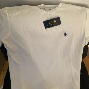 Vit t-shirt från Polo Ralph Lauren - Klassisk vit t-shirt från Polo Ralph Lauren med liten broderad logga i marinblått på bröstet. Enkel och stilren design med rund hals och korta ärmar. Perfekt basplagg för garderoben.