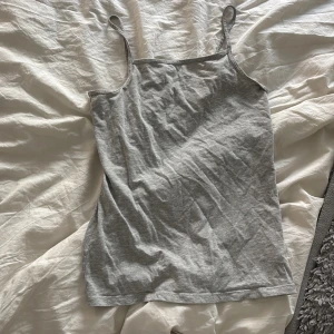 Grå linnetopp från H&M - Säljer en enkel och stilren grå linnetopp från H&M. Toppen har smala axelband och rak passform, perfekt att matcha med jeans eller kjol. Mjuk och skön bomullskänsla. Säljer en likadan i svart 