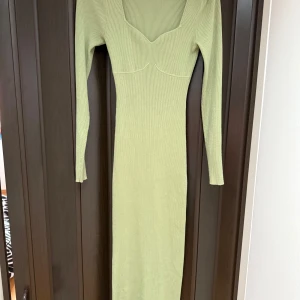 Ljusgrön ribbad långklänning från Adoore - Snygg ljusgrön långklänning från Adoore med ribbad struktur och lång ärm. Klänningen har en djup v-ringning och figurnära passform som framhäver siluetten. Perfekt för dig som gillar stilrena och trendiga plagg.