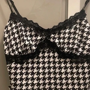 Spets linje  - Snygg svartvit linnetopp med ett klassiskt hundtandsmönster. Toppen har smala axelband och vacker spets längs kanterna. Perfekt för en stilren look.
