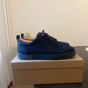 Mörkblå sneakers från Christian Louboutin - Snygga mörkblå sneakers från Christian Louboutin i mocka med den ikoniska röda sulan. Skorna har snörning och en stilren design som passar perfekt för en trendig look.