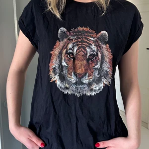 Svart t-shirt med tigertryck - Svart t-shirt med tigertryck och upprullade axlar från Vila. Storlek S.