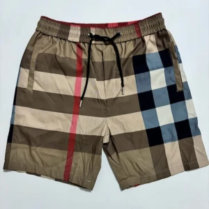 Rutig shorts från Burberry - Snygga shorts från Burberry med klassiskt rutigt mönster i beige, blått och rött. De har en elastisk midja med snörning för justerbar passform. Perfekta för en stilren och avslappnad look.