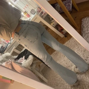 Ljusblå bootcut jeans - Säljer ett par ljusblå bootcut jeans med hög midja. De har en klassisk femficksdesign och en snygg utsvängd passform som ger en retro känsla. Perfekta för att skapa en avslappnad men stilren look.