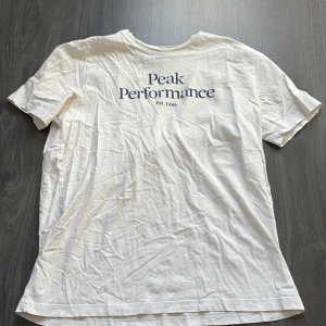 Vit t-shirt från Peak Performance - Säljer en klassisk vit t-shirt från Peak Performance med tryck 'Peak Performance Est. 1986' på framsidan. T-shirten är kortärmad och gjord i mjuk bomull. Tröjan är använd men inget som syns på så sätt. Märket har inga defekter 
