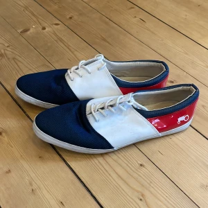 Flerfärgade sneaker - Unika sneakers i blått, vitt och rött med ett coolt traktortryck på sidan. Skorna har snörning och en rund tå, vilket ger en bekväm passform. Perfekta för dig som vill sticka ut med en färgglad och lekfull stil.