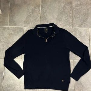 Mörkblå tröja med dragkedja - Säljer en stilren mörkblå tröja från Next med dragkedja vid halsen. Tröjan har långa ärmar och en klassisk krage med vita detaljer. Perfekt för en avslappnad men snygg look.