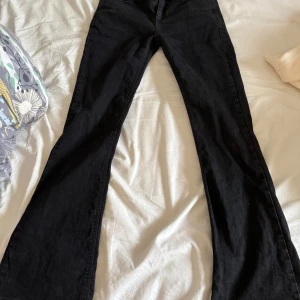 Lågmidjade Svarta bootcut jeans - Säljer ett par svarta bootcut jeans med klassisk femficksdesign och dragkedja. Byxorna har hög midja och är tillverkade i ett mjukt denimtyg som ger en snygg siluett. Perfekta för dig som gillar en tidlös look.säljs pg för små! 