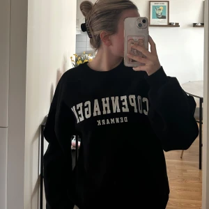 Svart sweatshirt med tryck från Gina tricot - Svart oversized sweatshirt med vit text 'Copenhagen Denimark' framtill. Tröjan har rund halsringning och långa ärmar. Perfekt för en avslappnad stil.