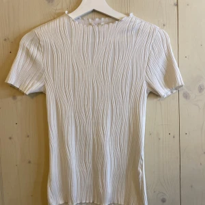 Vit ribbad topp från Amisu - Säljer en vit ribbad topp från Amisu i storlek XS. Toppen har korta ärmar och ett snyggt strukturerat tyg med vertikala ränder. Perfekt att styla till jeans eller kjol för en fräsch look.