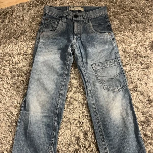 Blå jeansbyxor från Detroit - Snygga blå jeansbyxor från Detroit med klassisk femficksdesign och en extra ficka på ena benet. Byxorna har raka ben och normal passform, perfekta för en avslappnad stil. Stängs med knapp och dragkedja framtill.