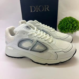 Vita Dior B30 sneakers  - Säljer ett par vita Dior B30 sneakers med reflekterande silverdetaljer och tydlig CD-logga på sidan och hälen. Skorna har en sportig design med meshpaneler och robust sula. Perfekta för dig som vill ha en exklusiv och trendig look.