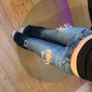 Blå slitna bootcut jeans - lågmidjade bootcut jeans med slitningar och hål på låren och knäna. de är även  slitningar på ena bakfickan