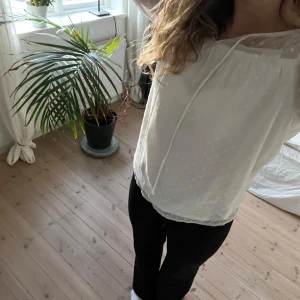 Vit blus med prickigt mönster från VILA - Säljer en söt vit blus från VILA med diskret prickigt mönster och transparenta partier upptill. Blusen har långa ärmar, knytband vid halsen och fina spetsdetaljer på axlarna.💕