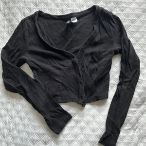 Svart croppad kofta - Snygg svart croppad kofta med knappar framtill. Perfekt för lager-på-lager-stil eller som ett lättare plagg för svalare dagar. Långärmad design som ger en stilren look.