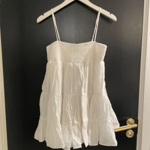 Vit klänning från Zara - Säljer en söt vit klänning från Zara med smala axelband och volangdetaljer. Klänningen har en smockad överdel och är perfekt för varma sommardagar. Den är luftig och bekväm att bära.