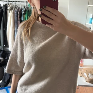 Beige stickad tröja med kort ärm - Mysig beige stickad tröja med rund halsringning och korta ärmar. Tröjan har en enkel och stilren design som passar perfekt till många olika outfits.