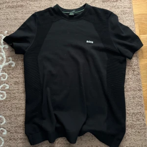 Svart t-shirt från BOSS - Säljer en svart t-shirt från BOSS med diskret logga på bröstet. T-shirten har korta ärmar och en klassisk passform. Perfekt för dig som gillar stilrena och enkla plagg.
