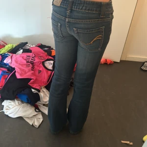 Blå bootcut jeans från Phink Industries - Säljer ett par klassiska blå jeans från Phink Industries med bootcut-modell. Jeansens gylf går dock inte att stänga den är sönder, men de märker man inte. Jeansen har snygga gula broderier på bakfickorna och kontrastsömmar. De har normal passform och är tillverkade i jeansmaterial med dragkedja och knapp. Skriv om ni vill veta midjemått eller har några andra funderingarn!!❤️