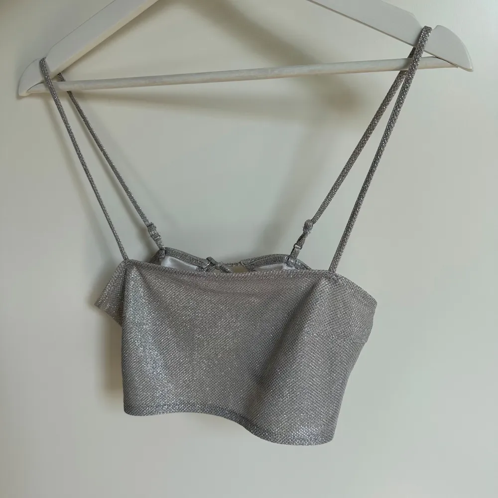 Säljer en glittrig silverfärgad croptop från H&M. Toppen har tunna axelband och knytning i ryggen för en snygg passform.. Yläosat.