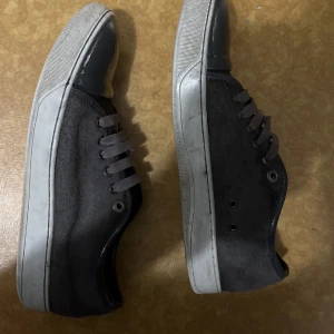 Svarta sneakers med grå sula - Säljer ett par svarta sneakers med grå sula och tå. Skorna har snörning och en klassisk, låg profil. Perfekta för vardagsbruk och passar till det mesta.