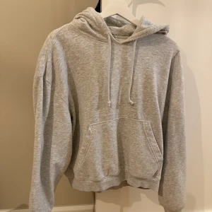 Grå hoodie från Weekday - Säljer en klassisk grå hoodie från Weekday i storlek XS. Tröjan har huva med dragsko, magficka och ribbade muddar. Perfekt för en avslappnad och stilren look.