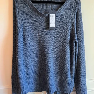 Grå stickad tröja från ONLY, ny med prislapp  - Säljer en stilren blå stickad tröja från ONLY. Perfekt för kyligare dagar med sin mjuka och bekväma passform. Tröjan har långa ärmar och en rund halsringning. Ett måste i garderoben för en avslappnad look.