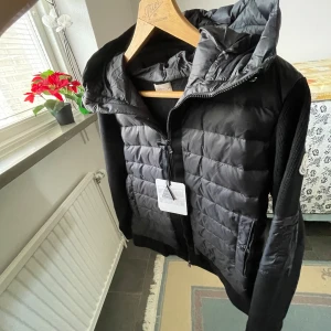 Svart dunväst från Moncler - Snygg svart dunväst från Moncler med dragkedja och huva. Perfekt för kyligare dagar med sin quiltade design. Västen har en stilren look och är lätt att matcha med olika outfits.                                            Storlek S. Passar till dig som väger runt 60-75kg.                                        NFC funkar