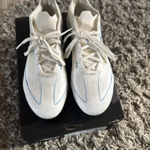 Vita fotbollsskor från Adidas nästa helt nya f50  - Snygga vita fotbollsskor från Adidas med blå detaljer och snörning. Perfekta för fotbollsplanen med en stilren design och bra grepp på sulan.