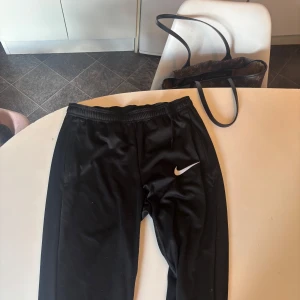 Svarta träningsbyxor från Nike - Säljer ett par svarta träningsbyxor från Nike med elastisk midja och det klassiska Nike-logotypen i vitt. Perfekta för träning eller en avslappnad dag.