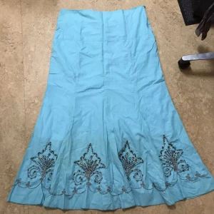 Ljusblå långkjol med broderi och pärlor - Ljusblå långkjol med utsvängd form och detaljerat broderi längs nederkanten. Kjolen har glittrande pärlor och paljetter i mönstret, vilket ger en unik och cool look. Perfekt för dig som vill sticka ut med något extra. Passar även 44 46.