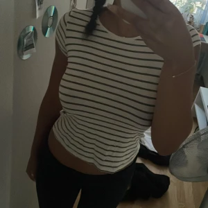 Randig t-shirt från H&M i bomull - Kortärmad t-shirt från H&M i vit med mörkgröna horisontella ränder. Gjord i mjuk ekologisk bomull, rund halsringning och figurnära passform. Perfekt för en chill och enkel stil. Knappt använd! 