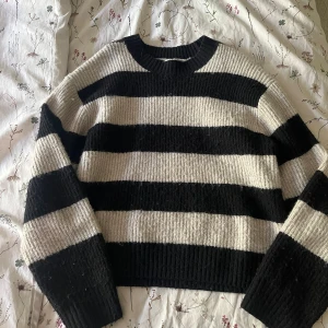 Randig stickad tröja i svart och beige - Säljer en mysig stickad tröja med breda svarta och beige ränder. Tröjan har rund halsringning, lång ärm. Perfekt att slänga på sig när det är kallt ute eller när man bara vill ha nått skönt på sig. 