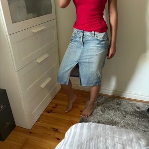 Ljusblå jeanskjol med slits - Snygg ljusblå jeanskjol med klassiska fickor fram och bak, bälteshällor och en cool slits framtill. Kjolen har en rak passform och går till knäna, perfekt för en chill och trendig look.