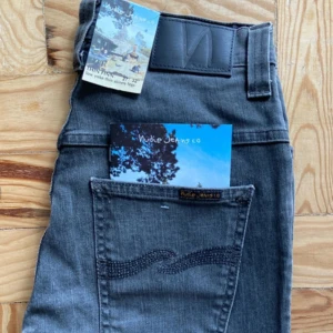 Gråa jeans från Nudie Jeans - Snygga gråa jeans från Nudie Jeans med klassisk broderad bakficka och svart läderpatch i midjan. Jeansen har låg midja och smal passform, perfekta för en stilren och modern look. Tillverkade i mjuk bomullsdenim.
