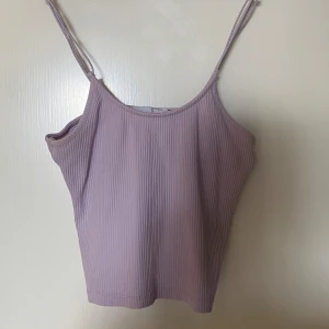 Ljuslila ribbad linnetopp  - Supersöt ljuslila ribbad linnetopp från 157 med smala axelband och croppad passform. Perfekt för dig som gillar en enkel men trendig look. Tunt och stretchigt material som känns skönt mot huden. Frakt tillkommer