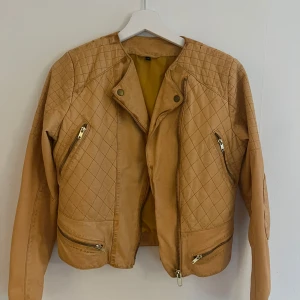 Beige quiltad skinnjacka stl 38 - Snygg beige skinnjacka med quiltade detaljer och dragkedjor framtill. Jackan har lång ärm, coola snedställda fickor och markerade axlar. Perfekt för dig som vill ha en edgy look med lite biker-vibe. Passar till både jeans och klänning.