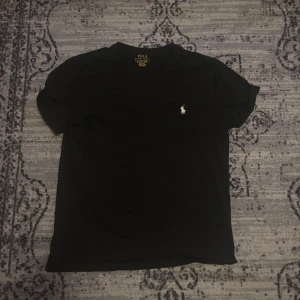 Svart t-shirt Polo Ralph Lauren - Svart t-shirt från Polo Ralph Lauren med klassisk vit broderad logga på bröstet. Modellen är slim fit och har rund halsringning och korta ärmar. Tillverkad i mjuk bomull som känns skön mot huden. Perfekt för en clean och stilren look.