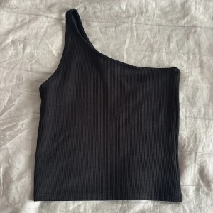 Svart ribbad oneshoulder topp - Snygg svart ribbad topp med oneshoulder-design. Den är lite croppad och tajtare, den är väldigt basic men samtidigt snygg! Passar inte längre därav inga bilder på❣️