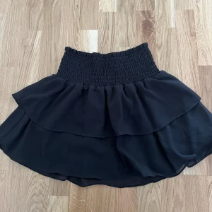 Svart volangkjol från Chelsea - Supersöt svart kortkjol från Chelsea med bred smock i midjan och dubbla volanger. Kan användas till både en topp eller en kjol!✨