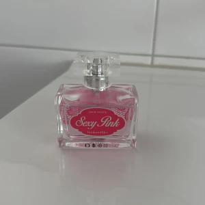 Sexy Pink parfym från Hunkemöller - Parfymen Sexy Pink från Hunkemöller i en snygg, rektangulär glasflaska med rosa etikett och spetsmönster. Innehållet är ljusrosa och flaskan har en transparent fyrkantig kork. Rymmer 50 ml och är en eau de toilette.
