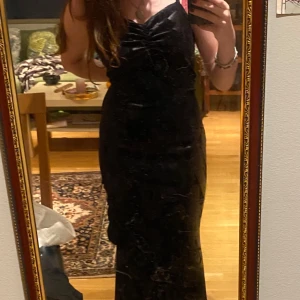 Svart mönstrad klänning - Svart lång mönstrad klänning i något sammets liknande material(syntetiskt) men väldigt stretchigt, den har även volanger nertill. Fick av en vän för väldigt länge sedan och har aldrig använt den, kan vara från Shein men vet inte så säljer den billigt. Den är alldeles för stor för mig så jag håller den i midjan i första bilden för att visa hur den hade sett ut på. Jättebra skick och som sagt knappt använd!