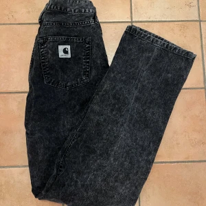 Svarta straight jeans från Carhartt - Säljer ett par svarta jeans från Carhartt med rak passform och hög midja. Storlek 25. Jeansen har klassisk femficksdesign, Carhartt-logga på bakfickan och är tillverkade i robust denim. Använda en del men fortfarande i fint skick och utan skavanker. Säljer eftersom de är för korta på mig. 