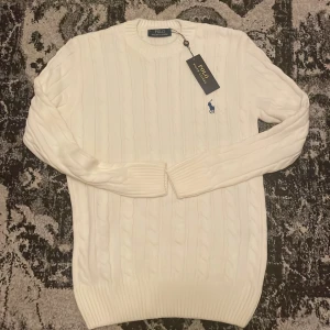 Vit kabelstickad tröja Polo Ralph Lauren - Vit kabelstickad tröja från Polo Ralph Lauren med klassisk rund halsringning och blå broderad logga på bröstet. Perfekt nu för vinter och hösten. Felfritt dock är den för stor för mig så behöver tyvärr sälja den. Priset är inte hugget i sten så kom med försläg och glöm inte att skriva ifall ni har fler frågor.
