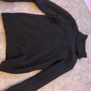 Svart stickad polotröja - Klassisk svart stickad polotröja med lång ärm och ribbade muddar vid hals, ärmslut och nederkant. Perfekt för lager-på-lager och enkel att matcha med allt. Tidlös och stilren modell som funkar året runt.