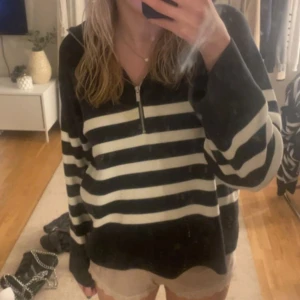 Randig svartvit tröja med half zip - Snygg svart och vit randig tröja med halv dragkedja framtill. Tröjan har en avslappnad passform och långa ärmar, perfekt för en chill och stilren look. Passar bra till jeans eller shorts för en casual vibe.