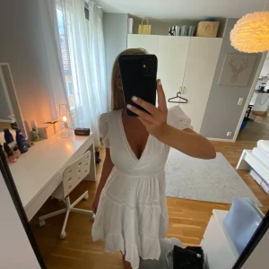 Vit kort omlottklänning med spets - Superfin vit kortklänning med omlott och djup v-ringning. Klänningen har puffiga korta ärmar, spetsdetaljer och volanger i kjolen. Lätt och luftig, perfekt för varma dagar. 