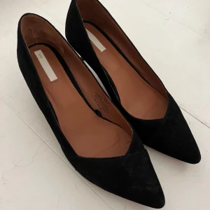 Svarta mockapumps från H&M, storlek 39  - Klassiska svarta pumps i mocka från H&M med spetsig tå och låg klack. Snygg och stilren design med skön innersula i skinn. Något dammiga. Köpta från Sellpy, säljer pga dem inte passade. 